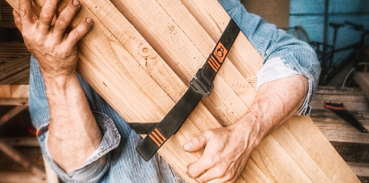 Un charpentier porte des planches de bois maintenues par une sangle Tybelt